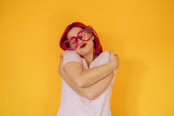 Smiling woman wearing heart shaped sunglasses hugging self