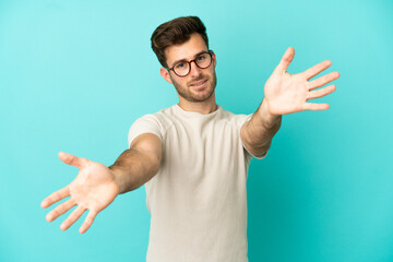 Fototapeta premium Young caucasian handsome man isolated on blue background presenting and inviting to come with hand