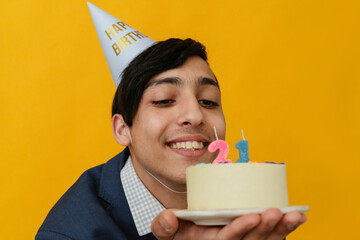 Happy man with party hat looking at 21st birthday cake