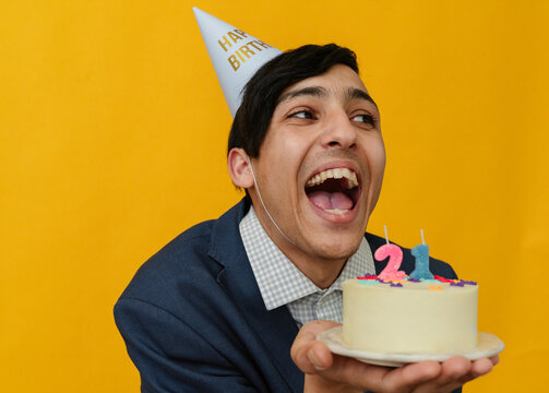 Cheerful man holding 21st birthday cake in studio