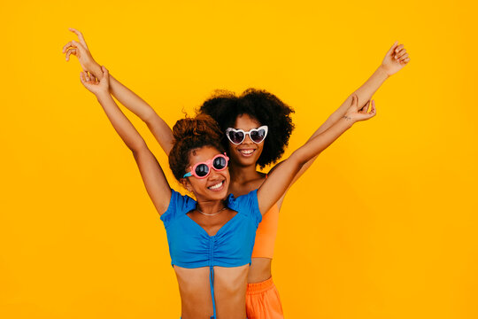 Carefree friends with arms raised against yellow background