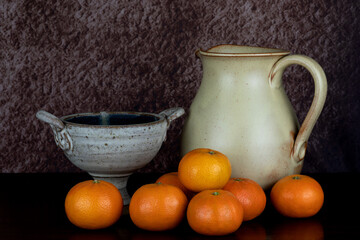 Earthenware Chalice Bowl and Wine Jug with Satsuma Oranges on a Wooden Surface - 670033975