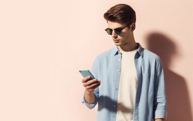 Portrait of a handsome man with sunglasses using smartphone, cellphone for online shopping, education, learning, texting on a pastel background. Copy space for text, advertising, message, logo