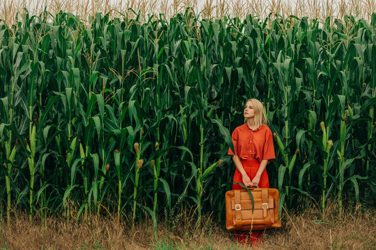 Woman carrying suitcase in corn field