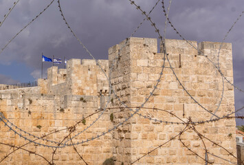 The Israel flag and Jerusalem Old Town tower and wall behind the barbed wire.