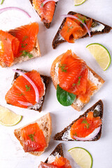 Bruschetta set with smoked trout slices, cream cheese and capers on wheat and rye bread. Flat lay with appetizers on white