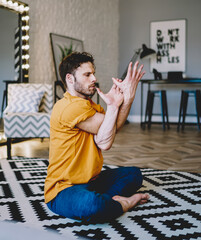 Calm young man practicing asana during sportive exercises in apartment