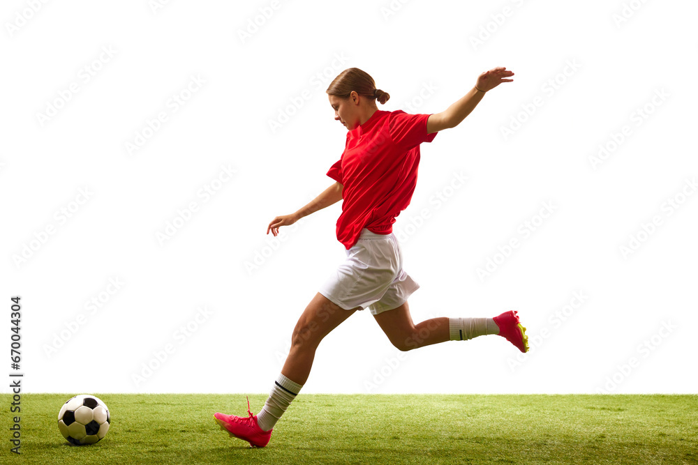 Wall mural Young athletic girl, football player in motion, playing on green grass, ready to hit ball isolated on white background. Concept of sport, competition, action, success, motivation. Copy space for ad