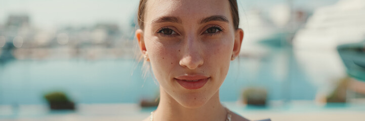 Smiling woman posing for the camera in the sea port. Girl enjoys a warm sunny day on background of yachts and ships