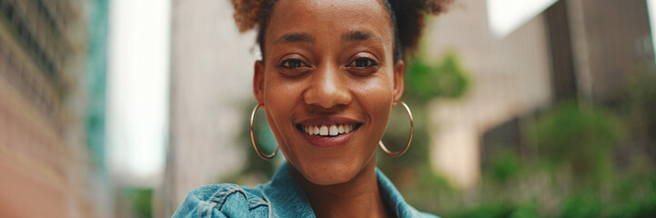 Closeup portret cute African girl with ponytail, wearing denim jacket makes stream, video call on smartphone in modern city background. © Andrii Nekrasov