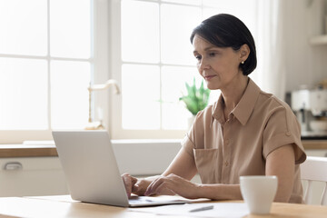 Serious middle-aged woman working at home use laptop, prepare report, makes on-line payment through...