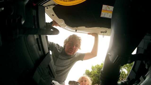 Worried father and cheerful little daughter open hood of their broken car