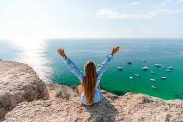 Woman travel sea. Happy woman in a beautiful location poses on a cliff high above the sea, with...