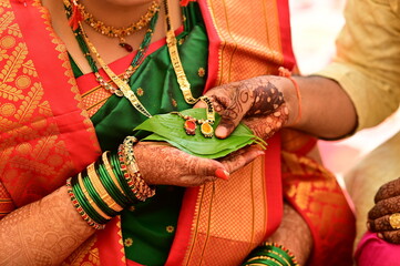 hands holding golden mangalsutra on leaf. Wedding indian jewelery. Bride and groom hands in mangalsutra ceremony. Henna hands. Indian wedding rituals. Maharashtra wedding