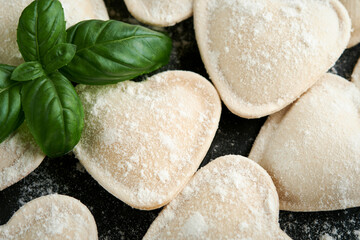 Fototapeta na wymiar Italian ravioli pasta in heart shape. Tasty raw ravioli with flour and basil on dark background. Food cooking ingredients background. Valentines or Mothers Day lunch ideas. Top view with copy space.
