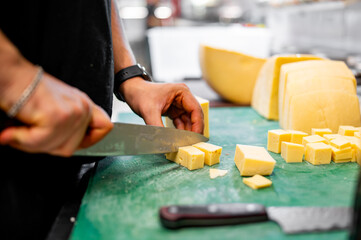 Obraz na płótnie Canvas man chef cutting cheese on dices with knife on kitchen