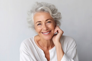 Portrait of beautiful mature woman with snow-white smile, gray hair on gray background. Middle-aged lady in light clothes, happy pensioner looking at the camera. Beauty, skin care concept