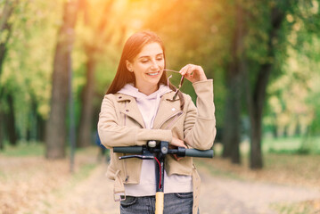 Young woman riding an electric scooter in an autumn park. Green transport, traffic jam problems.