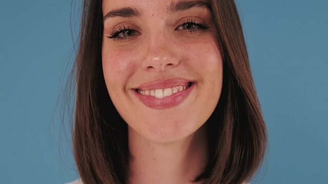 Close-up, young woman opens her eyes and looking at camera with smile isolated on blue background