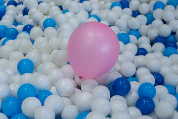 A pink balloon on top of blue and white plastic balls in ball pit at kids playground. Colorful plastic ball texture background. 