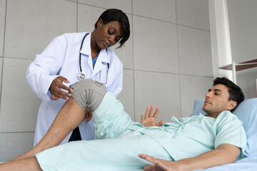 Obraz premium African American Doctor or Physiotherapist working examining treating of caucasian patient, leg stretching and exercise with wearing knee orthoses, in clinic 