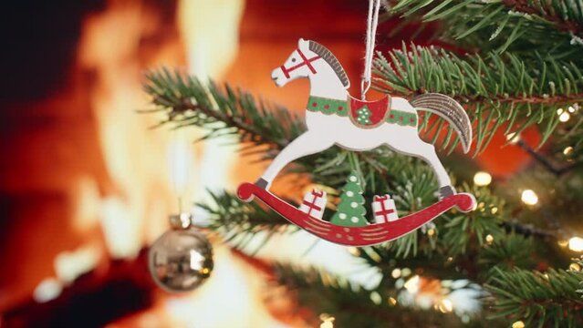 Christmas mood decoration wooden toy horse on Christmas tree rotate on branch of green spruce rotate blurred background of fireplace flame flickering light bulbs garlands family winter holiday Noel