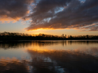 Obraz premium December sunrise at Draycote, Warwickshire, England, UK. Trees bare, apricot tinted clouds and reflections in the water. Rise and shine, it's time for a brand new day where anything could happen.