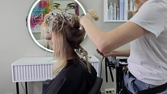  A hairdresser applies hair dye in the color of blonde to a young woman 