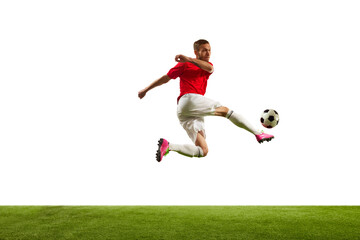 Full length portrait of professional soccer player kicking ball in motion against white background on green grass. Looks extremely motivated.