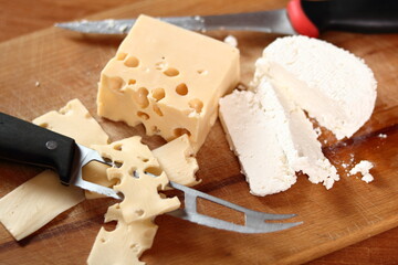 Slices of holey cheese and cottage cheese on wooden cutting board with knife
