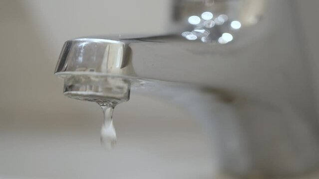 Water drops dripping from the bathroom faucet tap. Water leaking. Slow motion