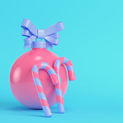 Pink christmas bauble with a bow and teo candy cane on bright blue background in pastel colors