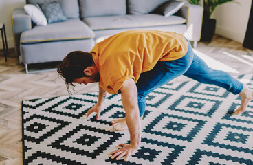 Young man practicing yoga poses on stylish carpet in modern apartment with home interior