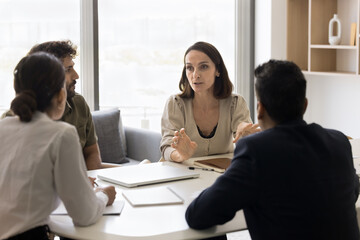 Mature businesswoman talking to team of colleagues on meeting, giving ideas for brainstorming on...