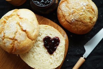 Freshly baked scones on a board next to a jar of jam and a knife on a dark background