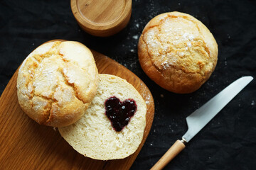 Freshly baked scones on a board next to a jar of jam and a knife on a dark background