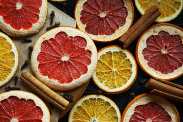 Dried orange and grapefruit slices on a wooden board next to cinnamon sticks and cloves on a dark...