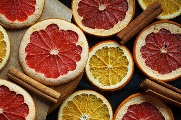 Dried orange and grapefruit slices on a wooden board next to cinnamon sticks on a dark background - obrazy, fototapety, plakaty