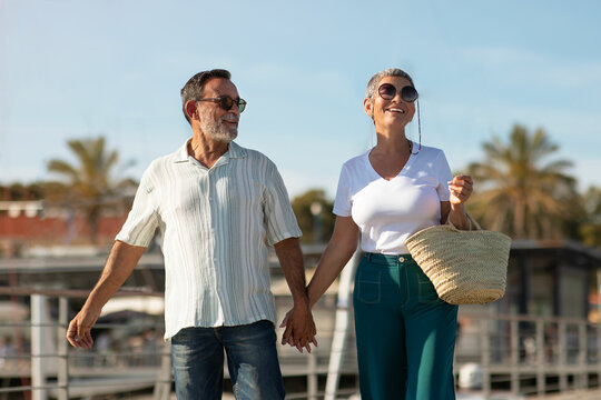 Senior romantic spouses holding hands posing at dock with sailboats