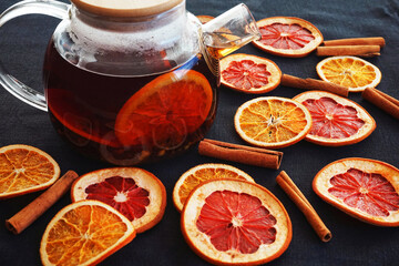 Glass teapot with black tea with orange next to dried orange and grapefruit slices on a dark...