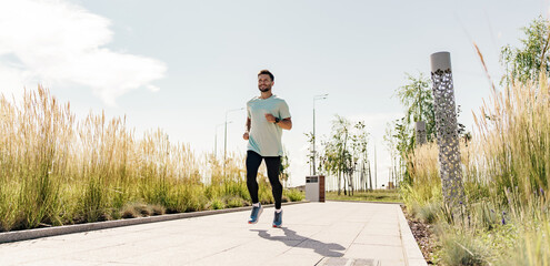 A man smiling warm-up runner in a T-shirt for active sports, rear view of a sunny day. Coach one trains with sportswear runs uses fitness watches.