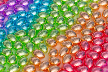 Many foil-wrapped chocolate eggs are arranged in rainbow color composition.