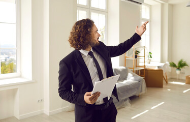 Real estate sales. Confident male real estate agent conducts inspection in apartment that is for sale. Millennial curly-haired real estate man with clipboard talks about advantages of this property.  - obrazy, fototapety, plakaty