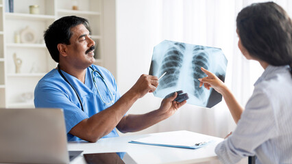 Middle aged indian doctor showing chest x-ray to female patient in clinic