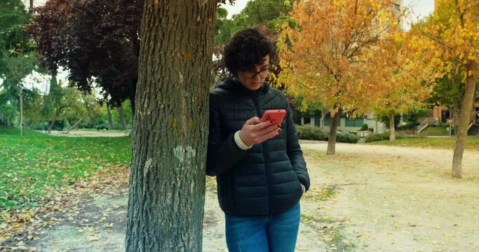 Woman using phone at a park by a tree