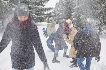 Group of young people are having fun enjoying game of snowballs, walking through winter...