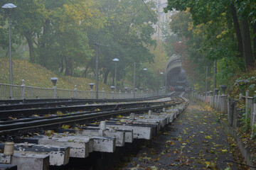 Detailed view railway for funicular cabin in Kyiv. Autumn colored trees in the park during rainy and foggy morning. Funicular is popular transport among locals and tourists. Travel and tourism concept