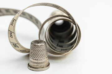 Horizontal photo, rolled sewing tape measure and thimble on white table Concept hobbies, handicrafts