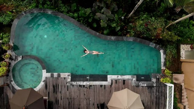 travel woman relaxing in infinity pool enjoying vacation lifestyle at luxury hotel spa with view of tropical jungle, drone view