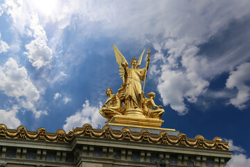 Fototapeta na wymiar Golden statue of Liberty on the roof of the Opera Garnier (Garnier Palace) against the sky with clouds. Sculpted by Charles Gumery in 1869. Paris, France. UNESCO World Heritage Site